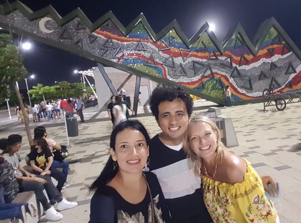 In a nighttime photo, travel blogger Kate Dana and two friends are seen with the Caiman sculpture on the Malecón del Rio in Barranquilla, Colombia ©Kate Dana